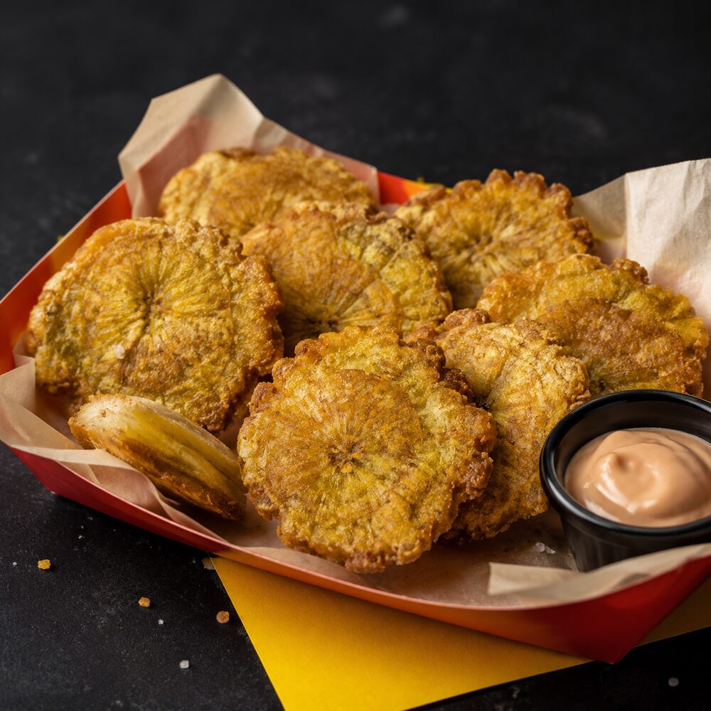 Twice-fried tostones in a red basket with a cup of pink dipping sauce
