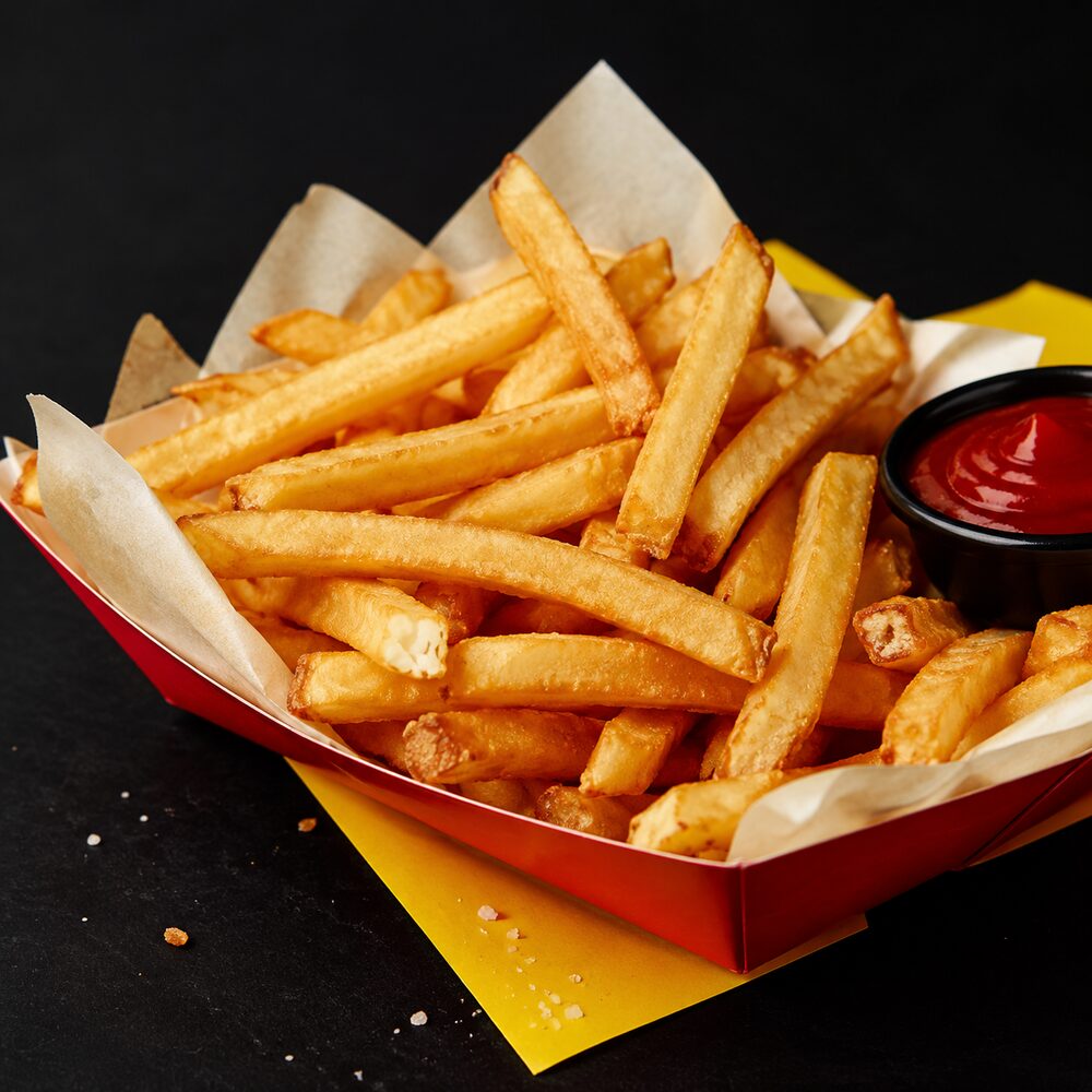 Thick-cut golden fries in a red basket with a cup of ketchup
