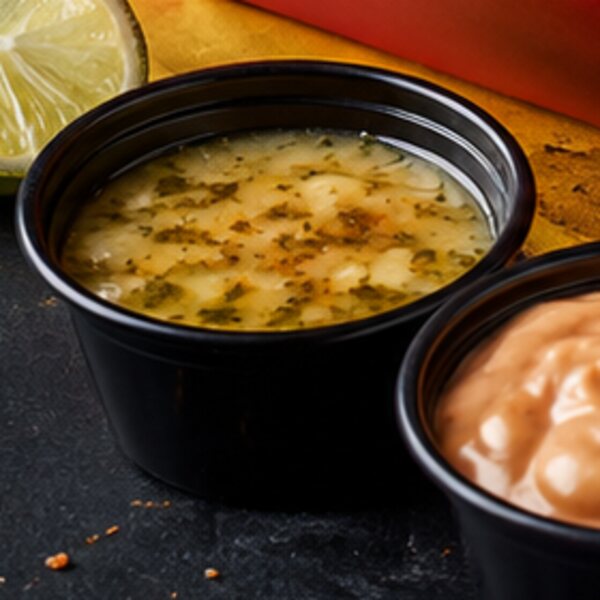 Close-up of a cup of wasakaka garlic-citrus sauce beside a lime wedge
